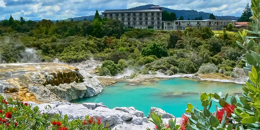 A bright blue thermal pool surrounded by white rock and greenery